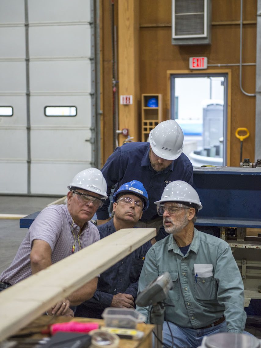 Four men in hard hats inspect a piece of Norway Spruce plywood.